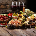 Italian antipasti wine snacks set. Cheese variety, Mediterranean olives, crudo, Prosciutto di Parma, salami and wine in glasses over wooden grunge background